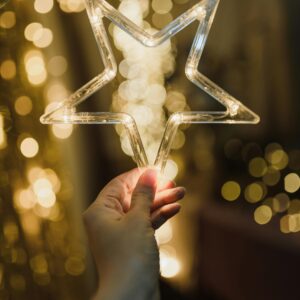 A hand holding a glowing star-shaped light against a backdrop of warm bokeh, perfect for festive moods.