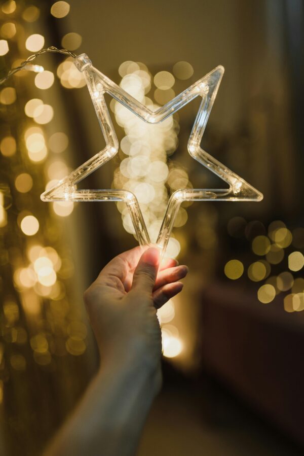 A hand holding a glowing star-shaped light against a backdrop of warm bokeh, perfect for festive moods.
